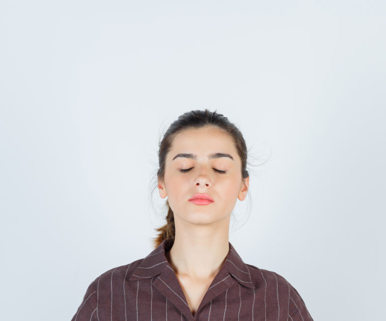 portrait of teenage girl showing mudra gesture shutting eyes in brown striped shirt and looking relaxed front view